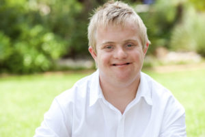 Close up portrait of boy with down syndrome in white shirt outdoors.